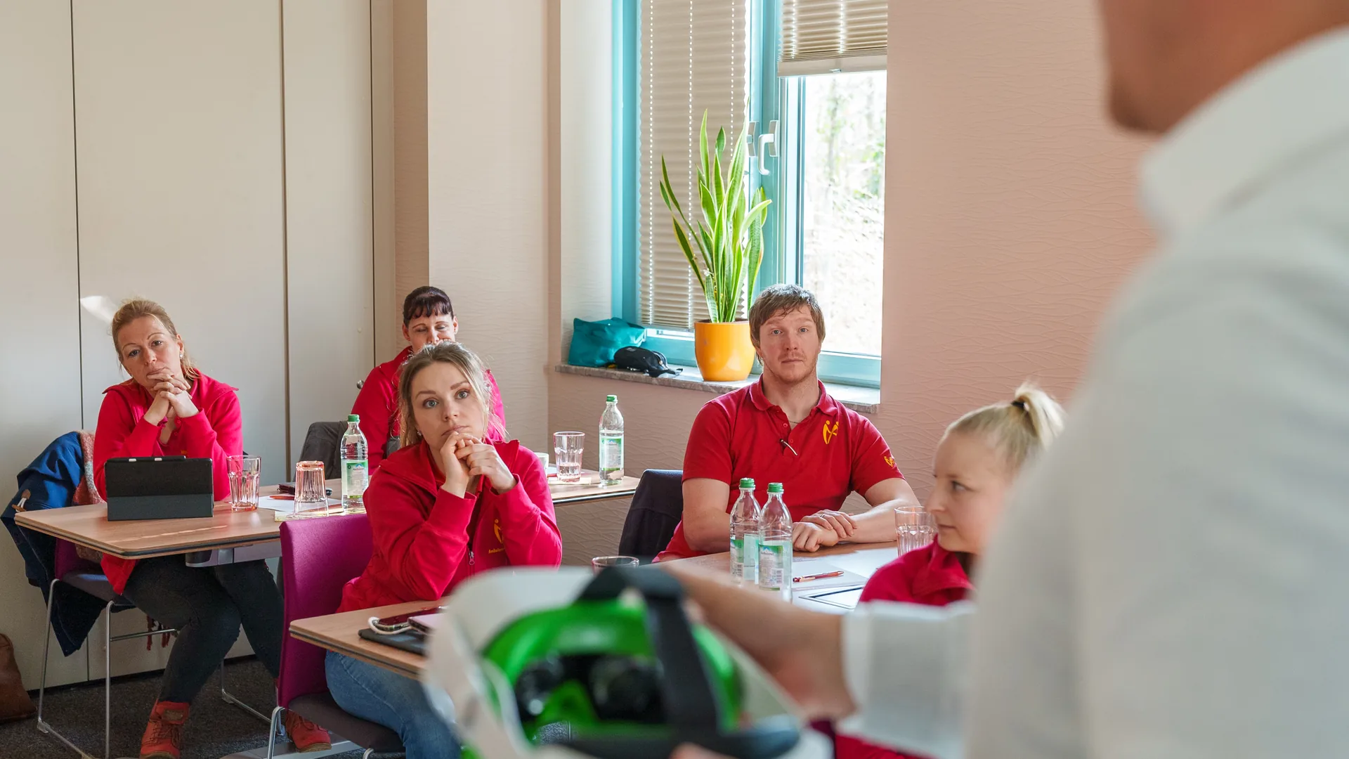 Mitarbeitende in roten Poloshirts hören bei einer internen Schulung zu